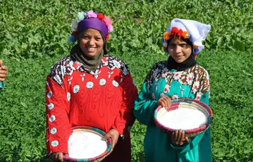Two agricultural workers holding baskets of white granular urea in a cultivated field